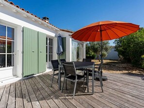 Una terraza de madera con una mesa, sillas y un paraguas, junto a una puerta verde.