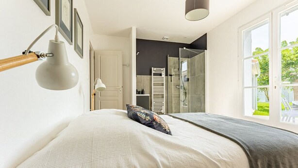 Un dormitorio con cama, lámpara de noche, ventana y puerta que da a un baño.