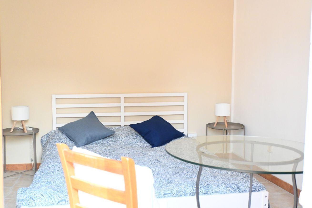 A bedroom with a bed, two bedside tables, a glass table, and a chair.