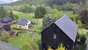A rural landscape with a large barn and several smaller buildings, surrounded by lush greenery and a forested hill in the background. - Ferien_Haus & Groß Grundstück in Bad Elster (Bad Elster)