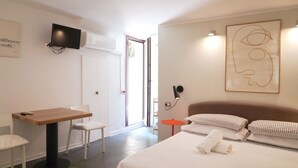Une chambre d’hôtel avec un lit, un bureau, une chaise, un téléviseur fixé au mur et un tableau.