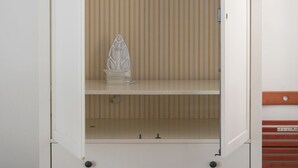 Une armoire blanche, avec un papier peint à rayures en arrière-plan et un objet décoratif posé sur l’étagère supérieure.