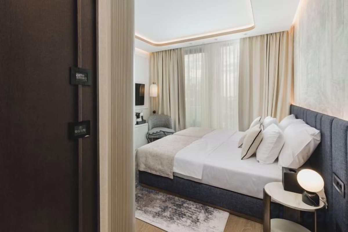 Habitación de hotel moderna con cama, mesita de noche, lámpara y cortinas.