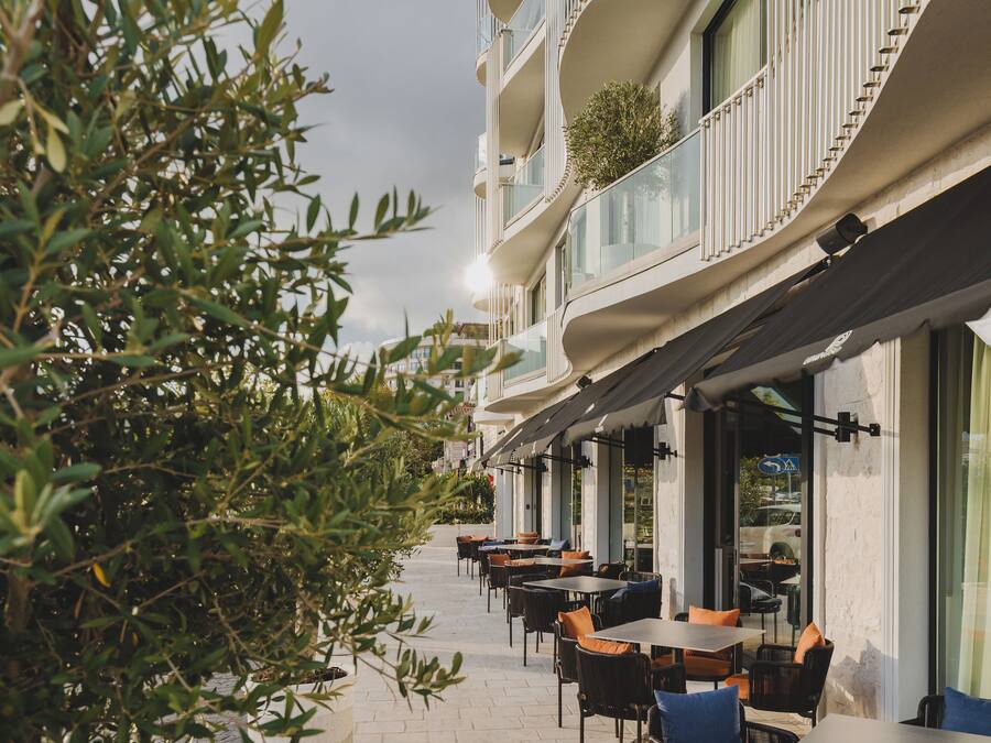 An outdoor seating area with tables and chairs, a pathway, and a building with balconies.