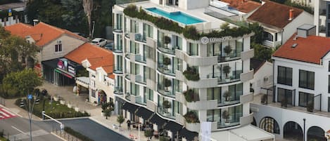 Un hotel moderno con piscina en la azotea, varios balcones y un patio con mobiliario de exterior.