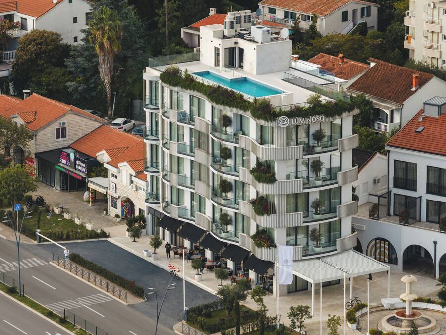 A modern hotel with a rooftop pool, multiple balconies, and a courtyard with outdoor seating.
