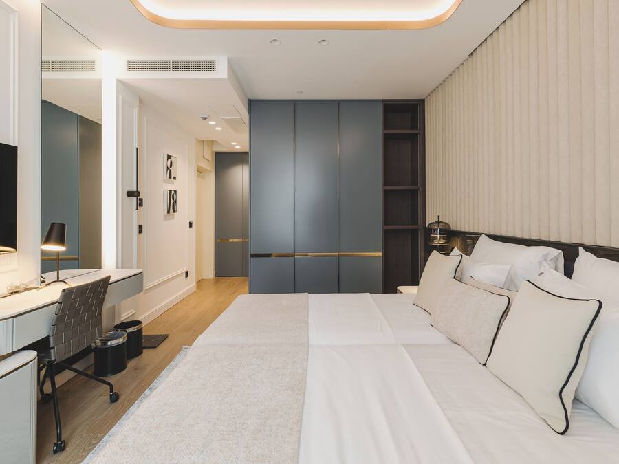 A modern hotel room with a large bed, a desk with a chair, a flat-screen TV, and a wardrobe.