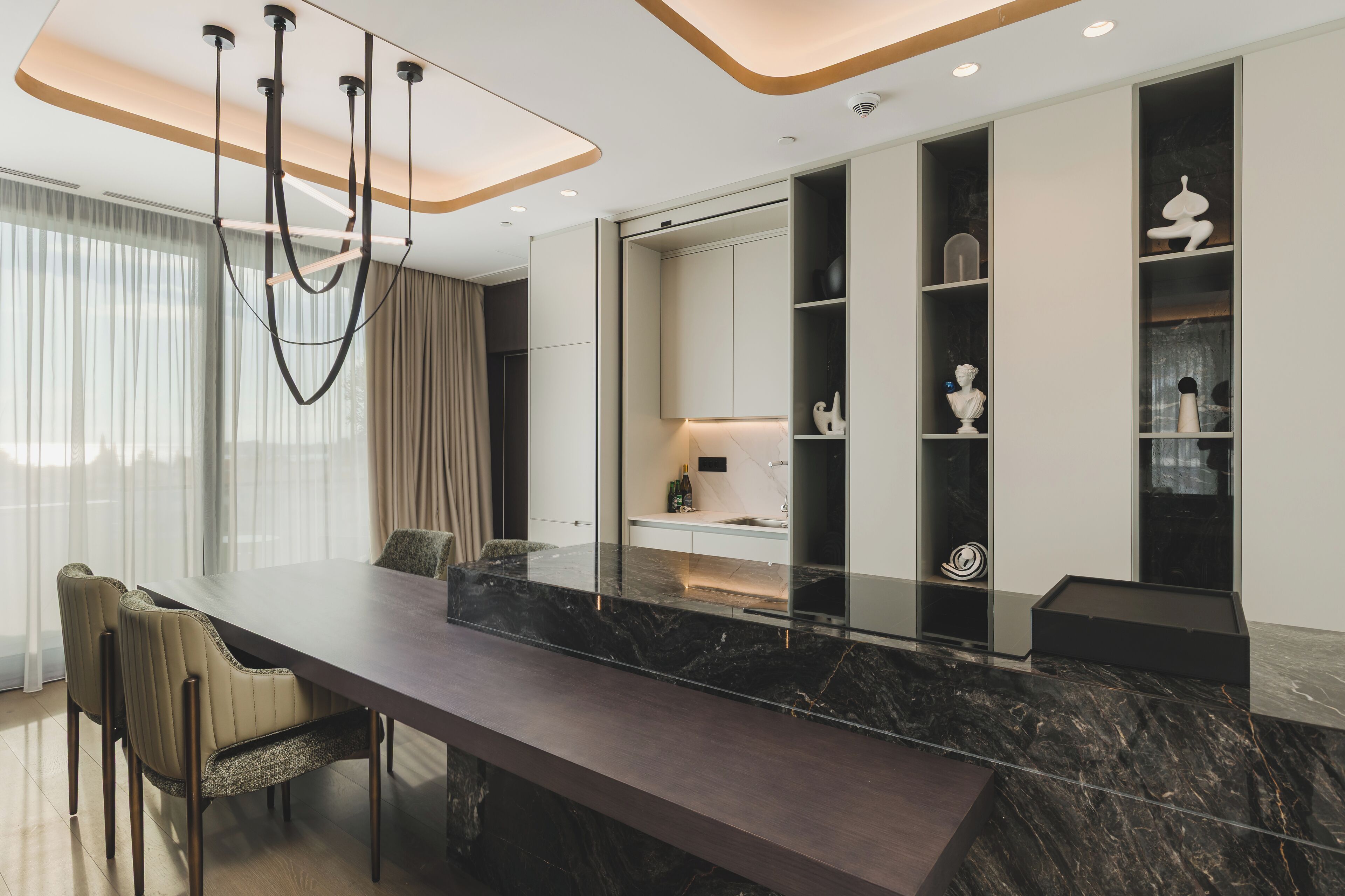 A modern dining area with a marble table, cushioned chairs, and built-in shelving with decorative items.