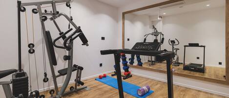 A gym with exercise equipment, a treadmill, and a mirror reflecting the space.