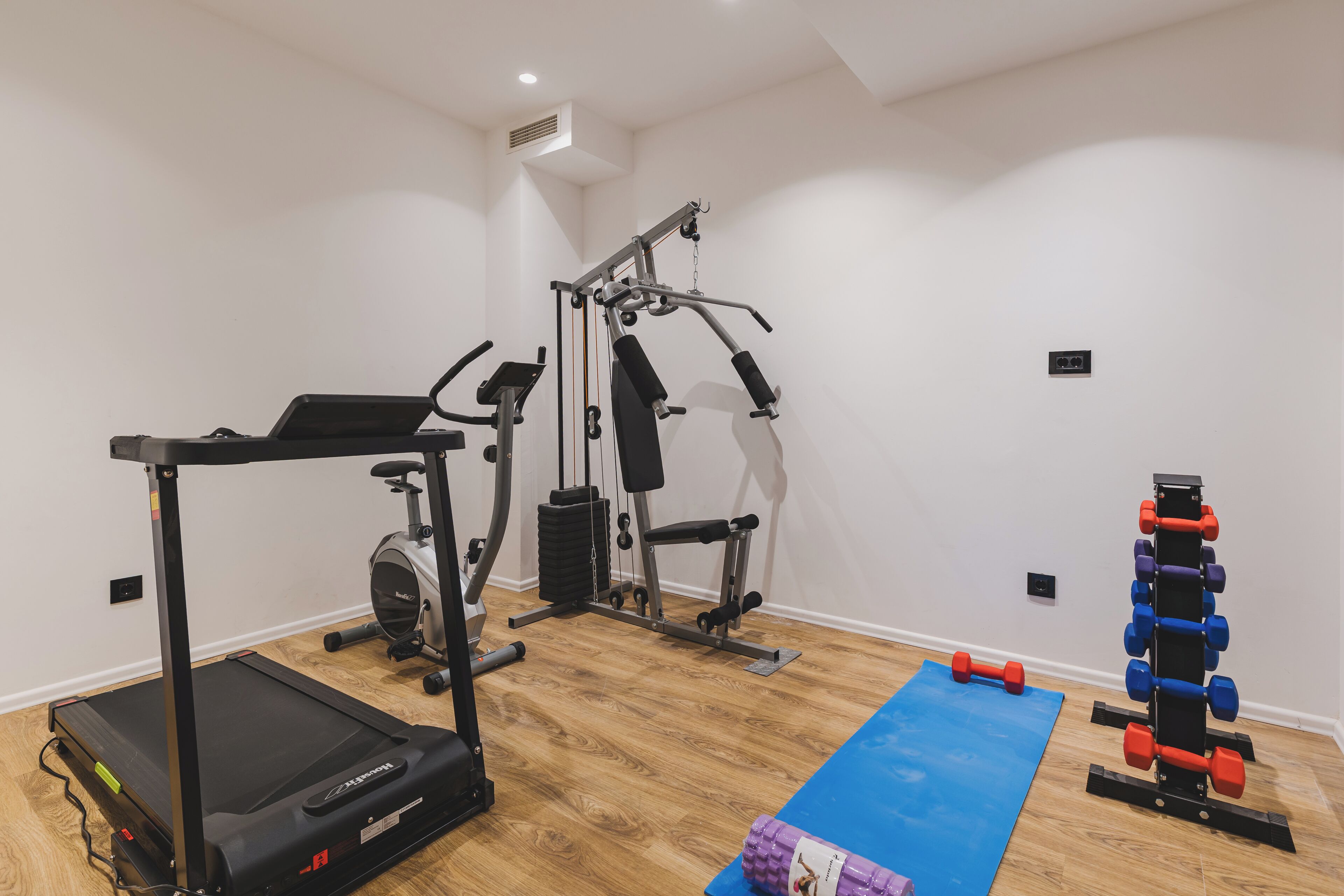 Un gimnasio en casa con cinta de correr, elíptica, banco de pesas y mancuernas.