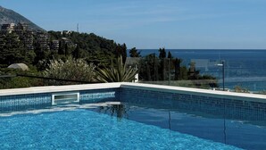 Ein klares, blaues Schwimmbecken mit Blick auf das Meer und Gebäude im Hintergrund.