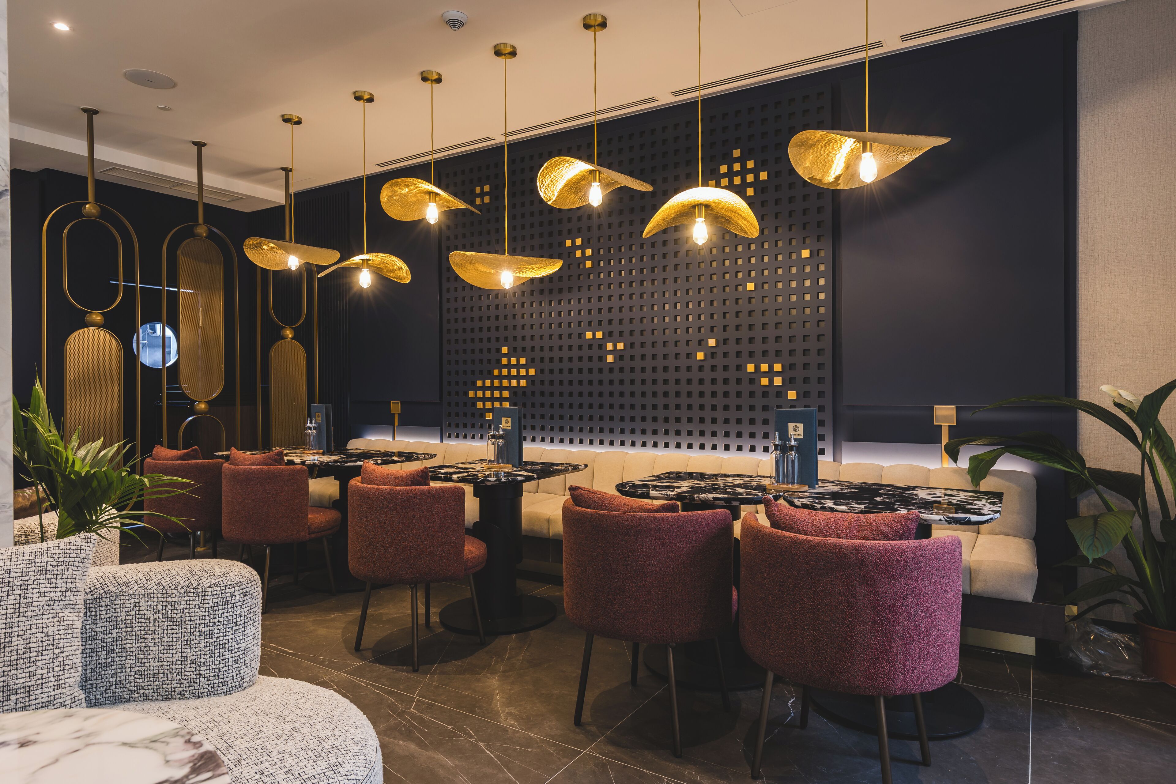 A modern restaurant interior with round tables, red upholstered chairs, and unique gold pendant lighting.