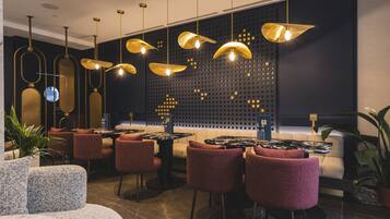 A modern restaurant interior with round tables, red upholstered chairs, and unique gold pendant lighting.