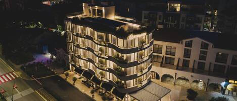 Un hotel de varios pisos con un diseño moderno, con balcones adornados con plantas, mobiliario exterior y una fuente.