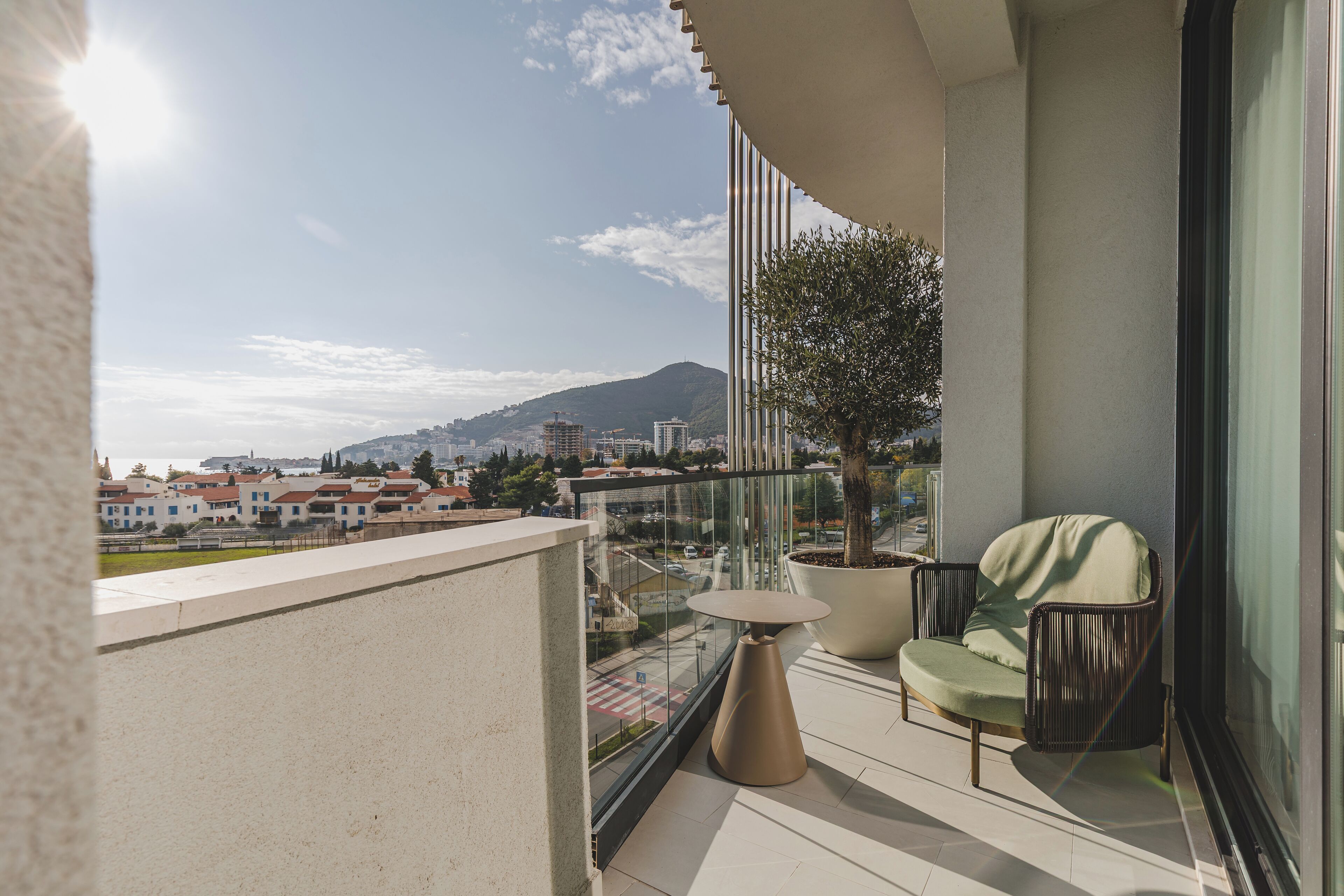 A balcony with a view of a cityscape, a potted tree, and a seating area with a table and chairs.