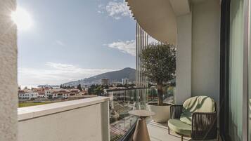 A balcony with a view of a cityscape, a potted tree, and a seating area with a table and chairs.