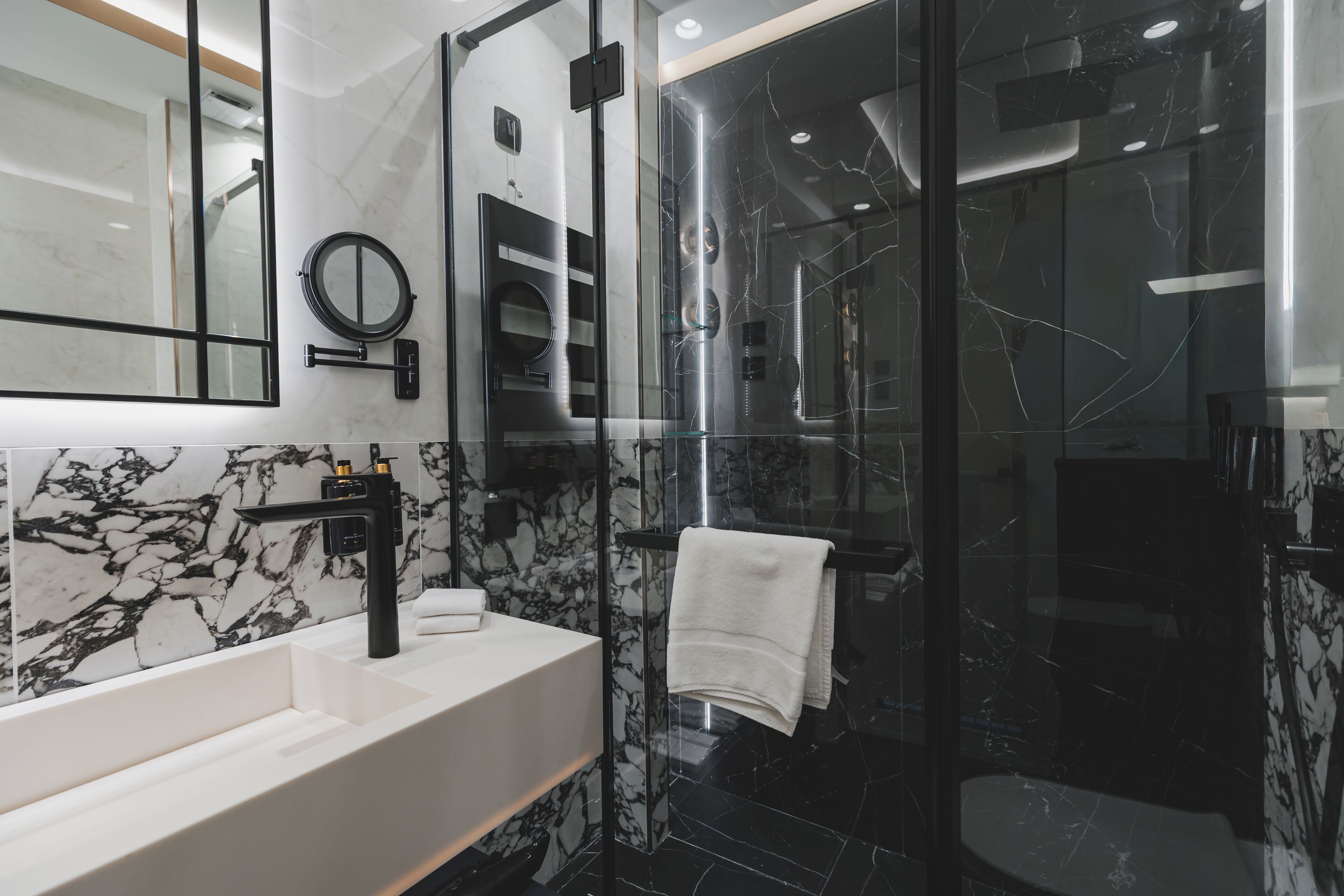 A modern bathroom with a large mirror, a black sink, and a glass-enclosed shower area.