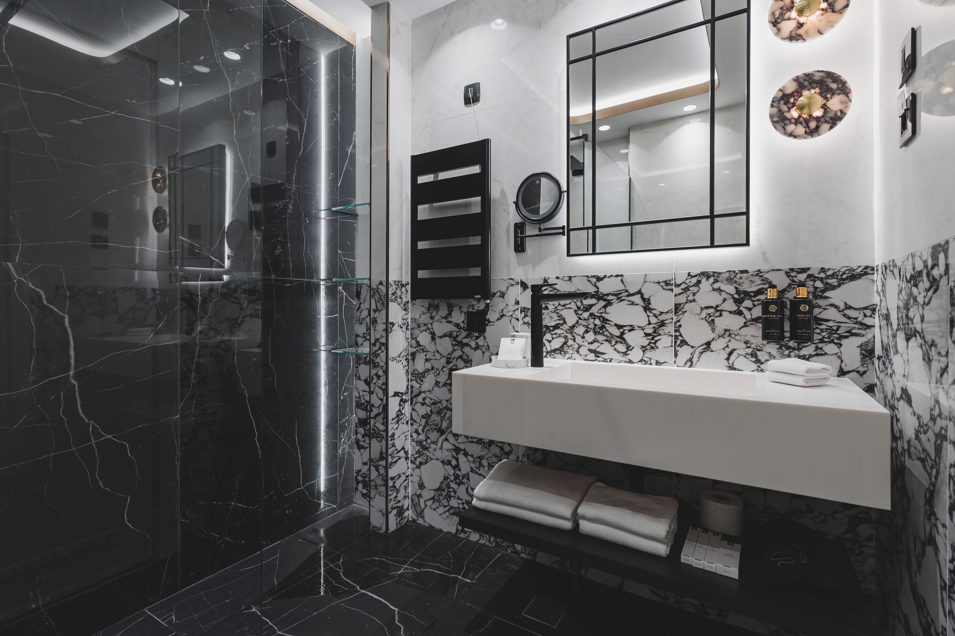 A modern bathroom with a glass-enclosed shower, a marble-tiled wall, a white sink, and a mirror above the sink.