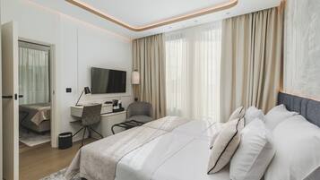 Una habitación de hotel moderna con una cama grande, un escritorio con silla, televisión y vistas a la ciudad a través de amplias ventanas.