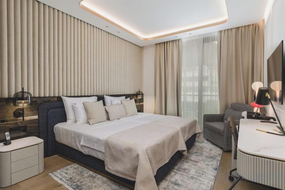 Una habitación de hotel moderna con una cama grande, mesitas de noche, un escritorio y un televisor.