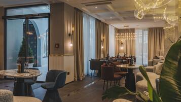A modern hotel lobby with a dining area, large windows, and a decorative chandelier.