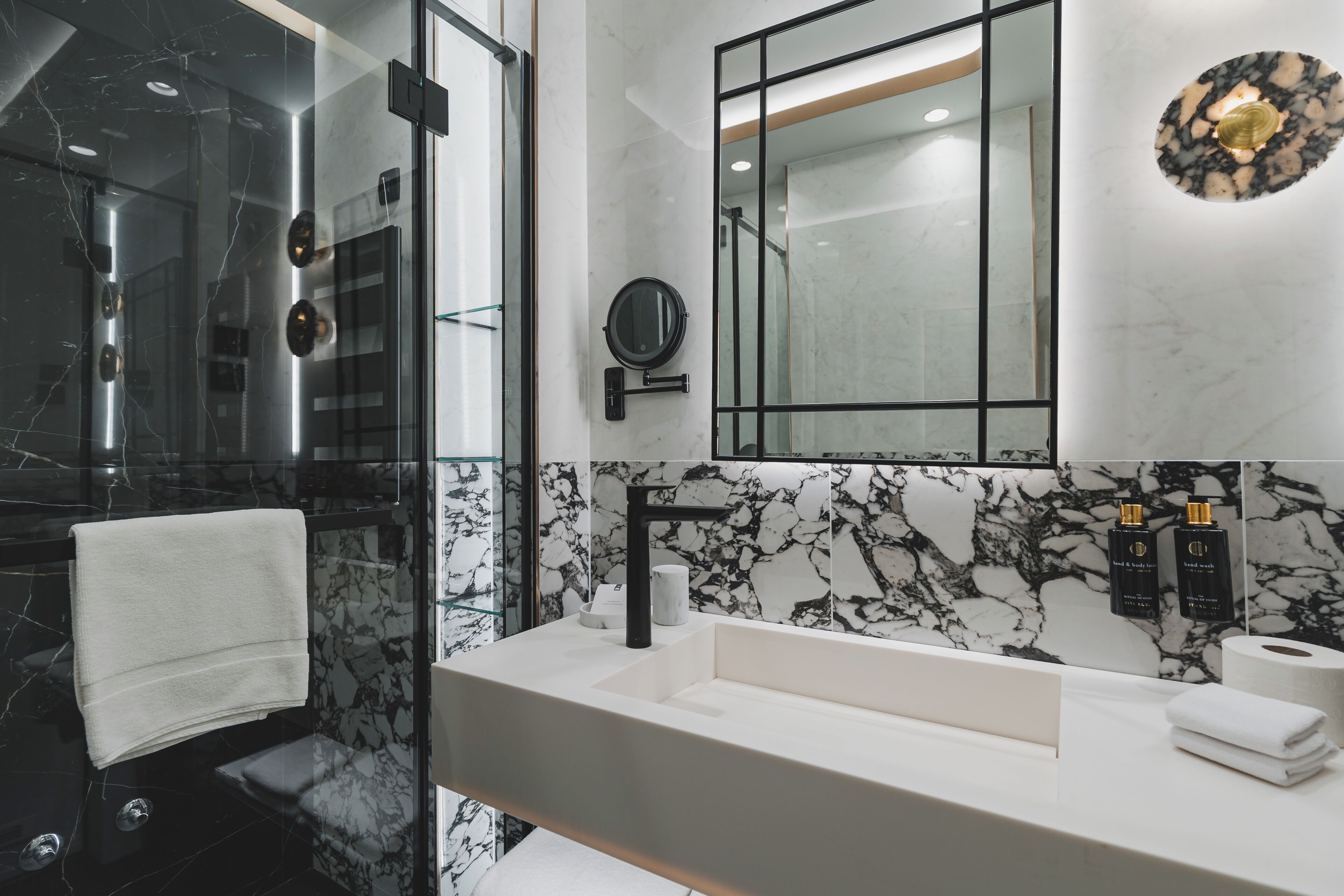 Un baño moderno con salpicadero de mármol, un espejo grande, un grifo negro y una mampara de cristal.
