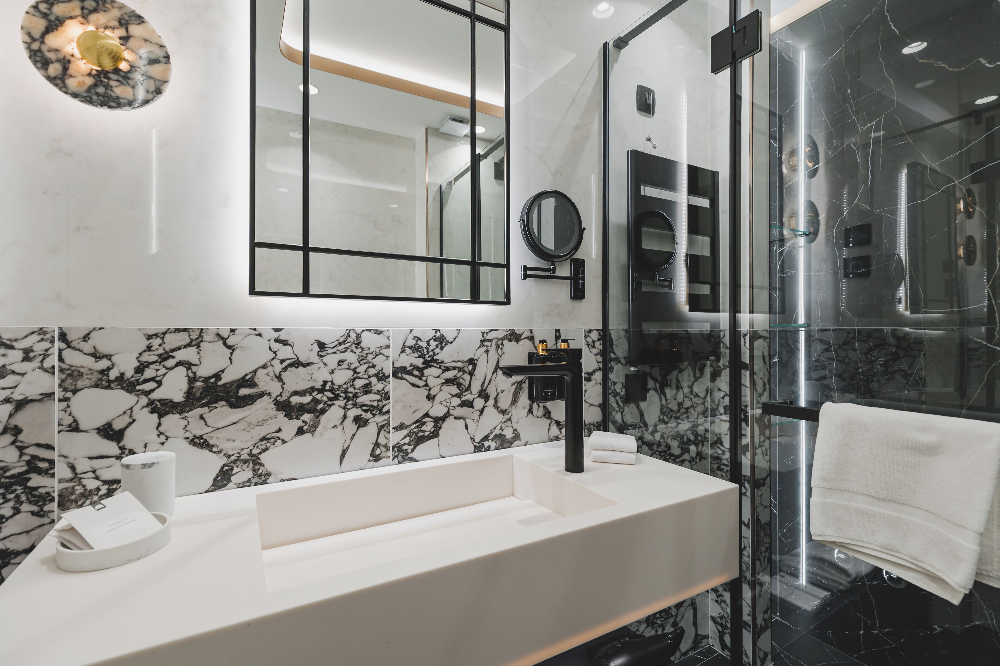 Un baño moderno con un lavabo blanco, accesorios negros y una cabina de ducha de vidrio.