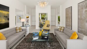A modern living room with a glass coffee table, two sofas, a yellow armchair, and a chandelier.