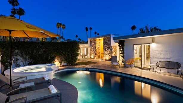 A modern outdoor pool area with lounge chairs, a hot tub, and a stone wall backdrop.