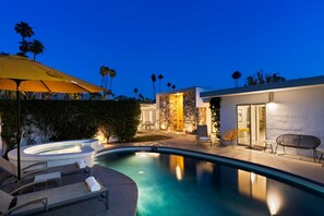 A modern outdoor pool area with lounge chairs, a hot tub, and a stone wall backdrop.