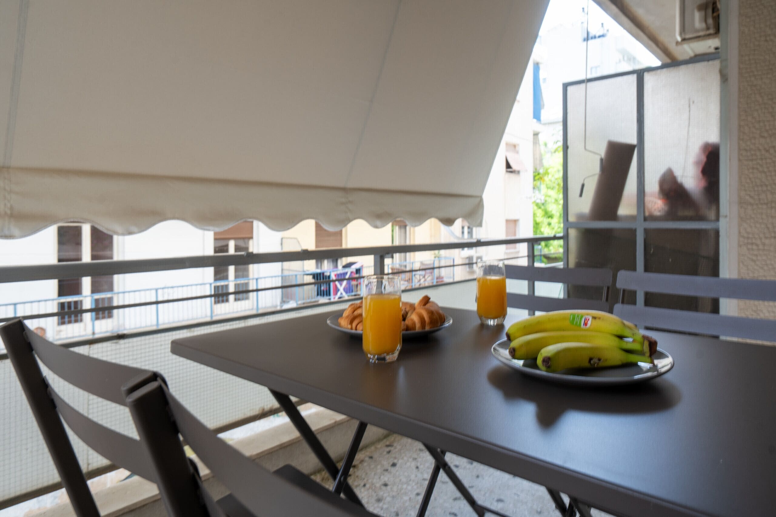 En balkon med et bord dækket til morgenmad, inklusive бананы, juice og bagværk.