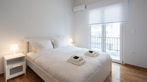 Une chambre à coucher au style minimaliste, avec un grand lit, du linge de lit blanc, deux tables de chevet avec des lampes et une vue à travers une porte-fenêtre coulissante.