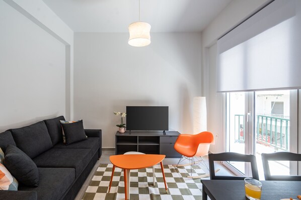 A modern living room with a black sofa, orange chairs, a flat-screen TV, and a checkered floor.