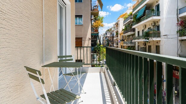 Un balcon étroit, agrémenté d’une table et de chaises, entouré d’immeubles dotés de balcons et de fenêtres.