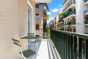 A narrow balcony with a table and chairs, surrounded by buildings with balconies and windows.