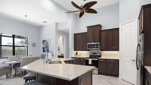 Una cucina moderna con mobili in legno scuro, una grande isola con sgabelli da bar, elettrodomestici in acciaio inossidabile e una ventola a soffitto.