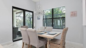 Un'area pranzo con un tavolo apparecchiato per quattro persone, circondata da sedie, un lampadario e ampie finestre che offrono vista sul verde circostante.