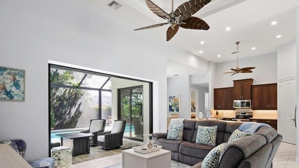 Un'ampia zona giorno con una grande finestra, un ventilatore a soffitto e una cucina sullo sfondo.