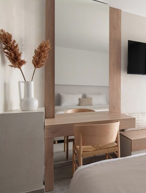 A modern bedroom with a wooden desk, a chair, a bed, and a TV mounted on the wall. - Olenia Suites (Neos Marmaras)