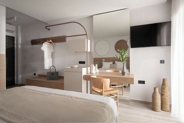 A modern hotel room with a bed, a desk, a mirror, and a TV. - Olenia Suites (Neos Marmaras)