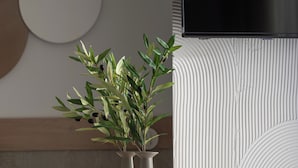 A modern interior with a wooden table, two vases with plants, and a wall-mounted TV. - Olenia Suites (Neos Marmaras)