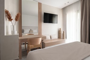A modern hotel room with a bed, a desk with a chair, a TV mounted on the wall, and a window with curtains. - Olenia Suites (Neos Marmaras)