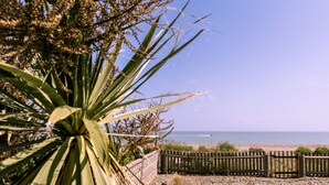 A beach view with a wooden fence, a palm tree, and a clear sky. - Beach Cottage with garden that blends into the beach in Pevensey Bay (Pevensey Bay)