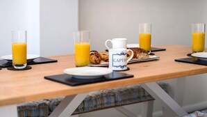 A breakfast setup with croissants, a coffee mug, and glasses of orange juice on a wooden table. - Beach Cottage with garden that blends into the beach in Pevensey Bay (Pevensey Bay)
