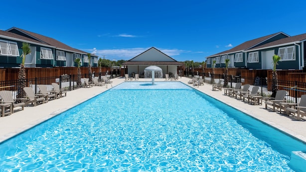En swimmingpool med solstolar och en byggnad i bakgrunden.
