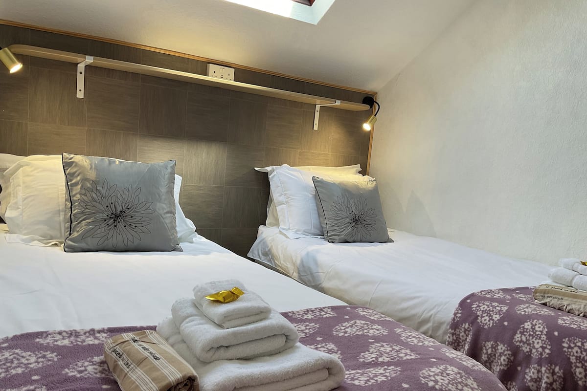 Ett hotellrum med två sängar, var och en med en sänggavel, ett litet takfönster och en prydligt vikt hög med handdukar på sängen.