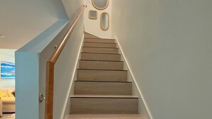 Eine Holztreppe mit Handlauf, weißen Wänden und einer Tür links.