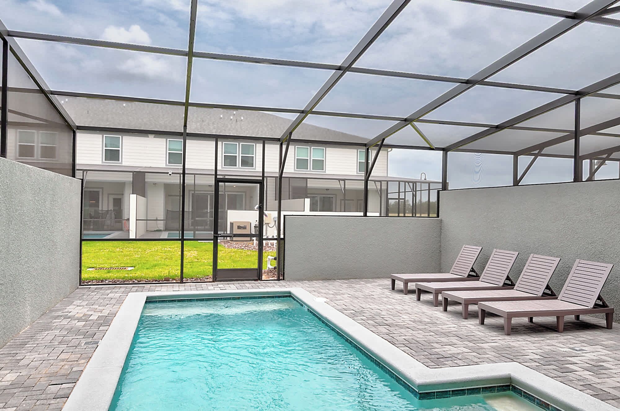 A swimming pool area with lounge chairs and a view of a house through a glass enclosure.