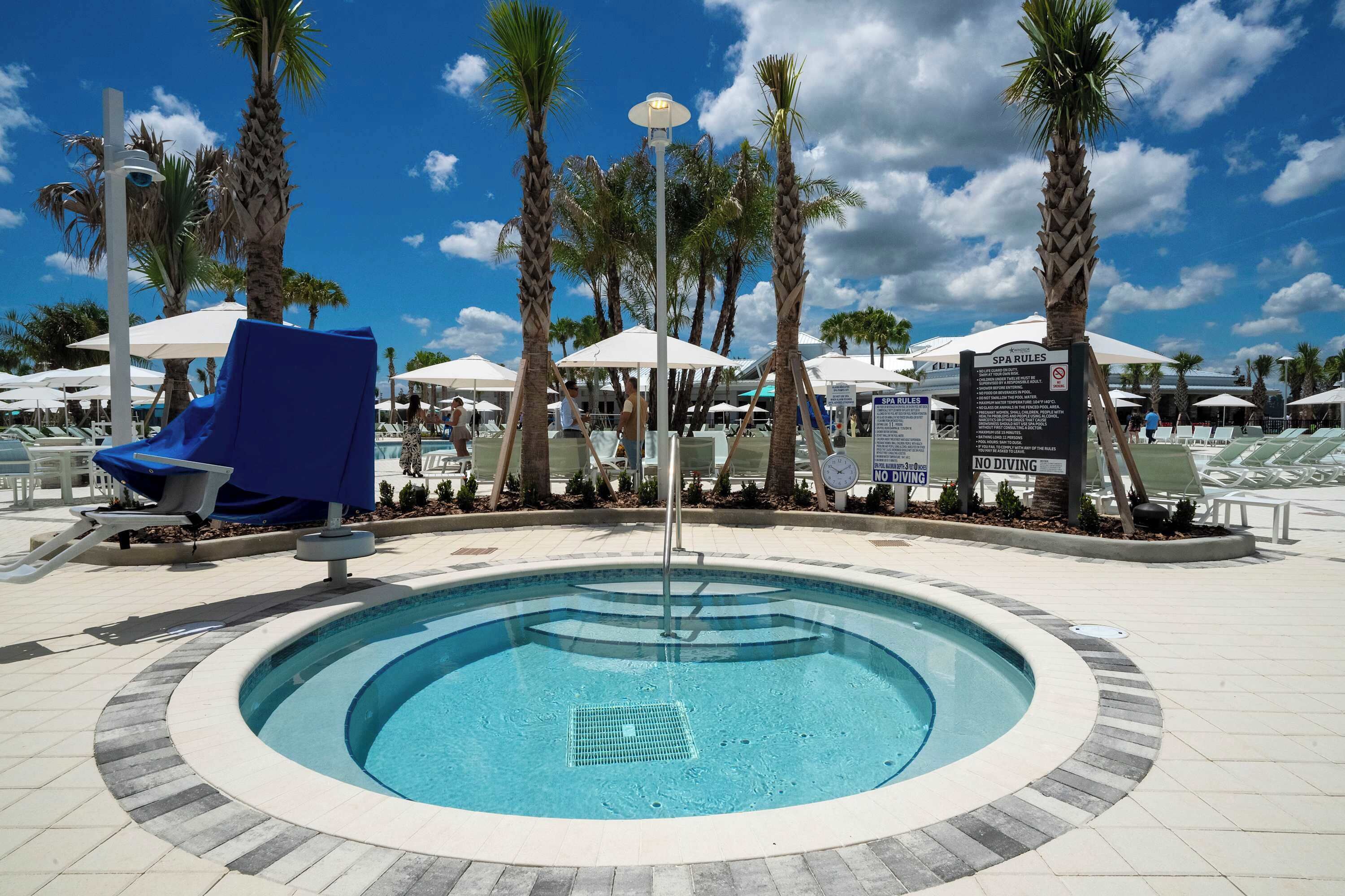A pool area with lounge chairs, umbrellas, and palm trees.