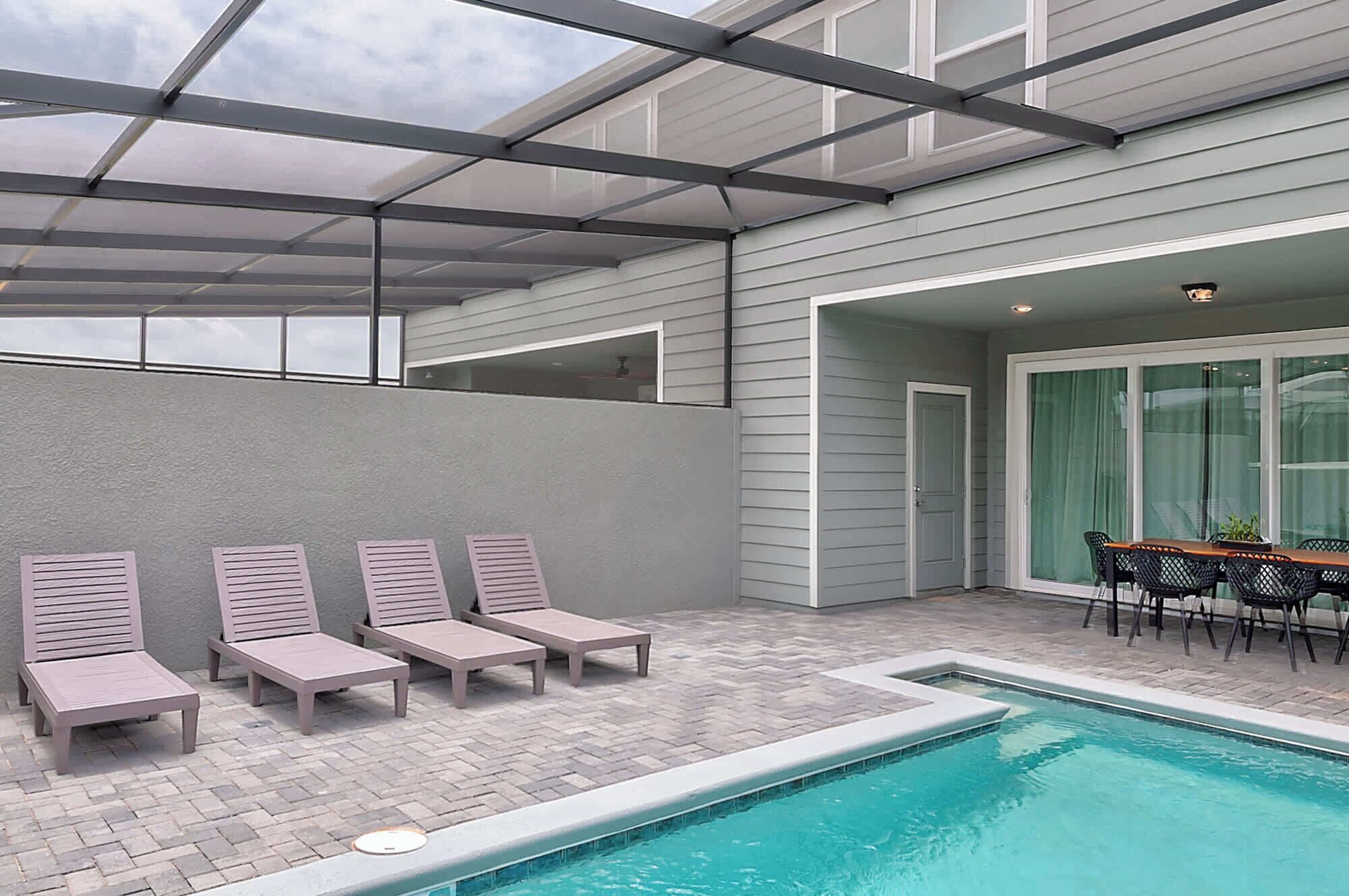 A pool area with lounge chairs, a table with chairs, and a glass door leading to a covered patio.